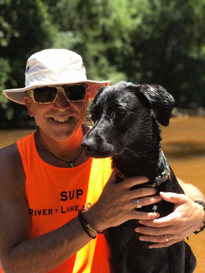 Miembro del equipo de paddle board YOLO sentado con su perro con Bomber gafas de sol flotantes de camuflaje