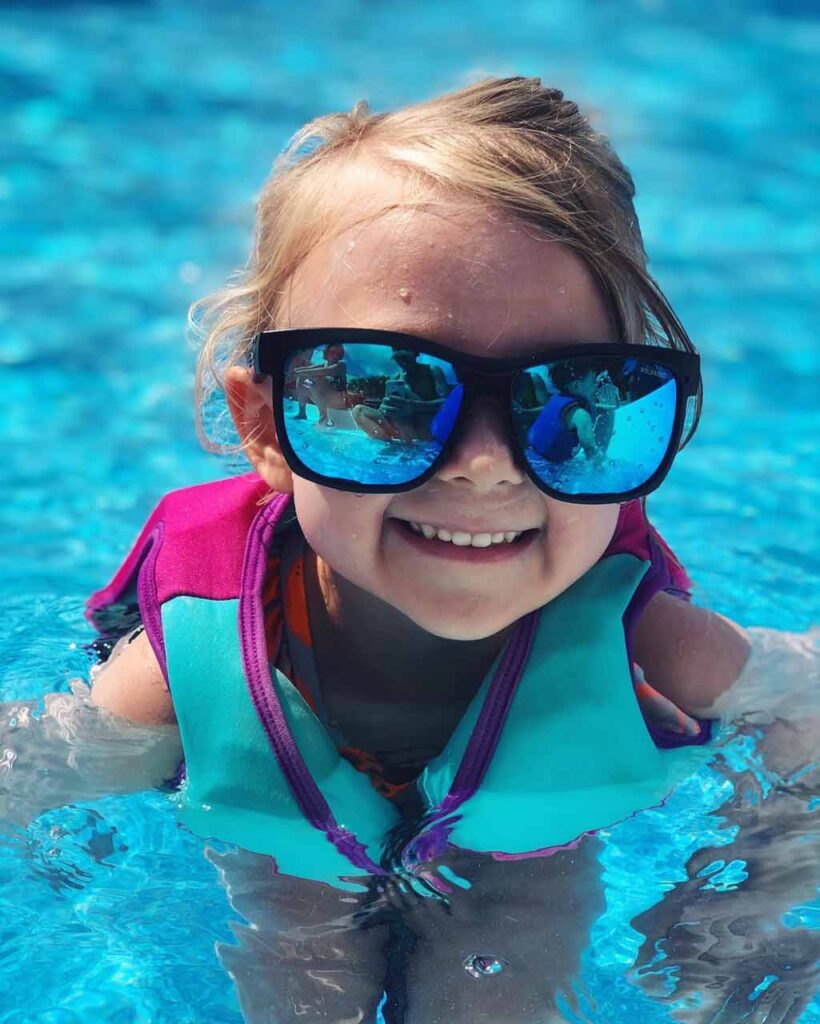 Linda niña vistiendo Bomber flotante gafas y un chaleco de seguridad en una piscina